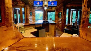 Interior de una cabaña de madera con una zona de bar, paredes de madera y dos televisores instalados en el techo.