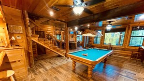 Un interior de madera con mesa de billar, escalera de madera y zona de bar.