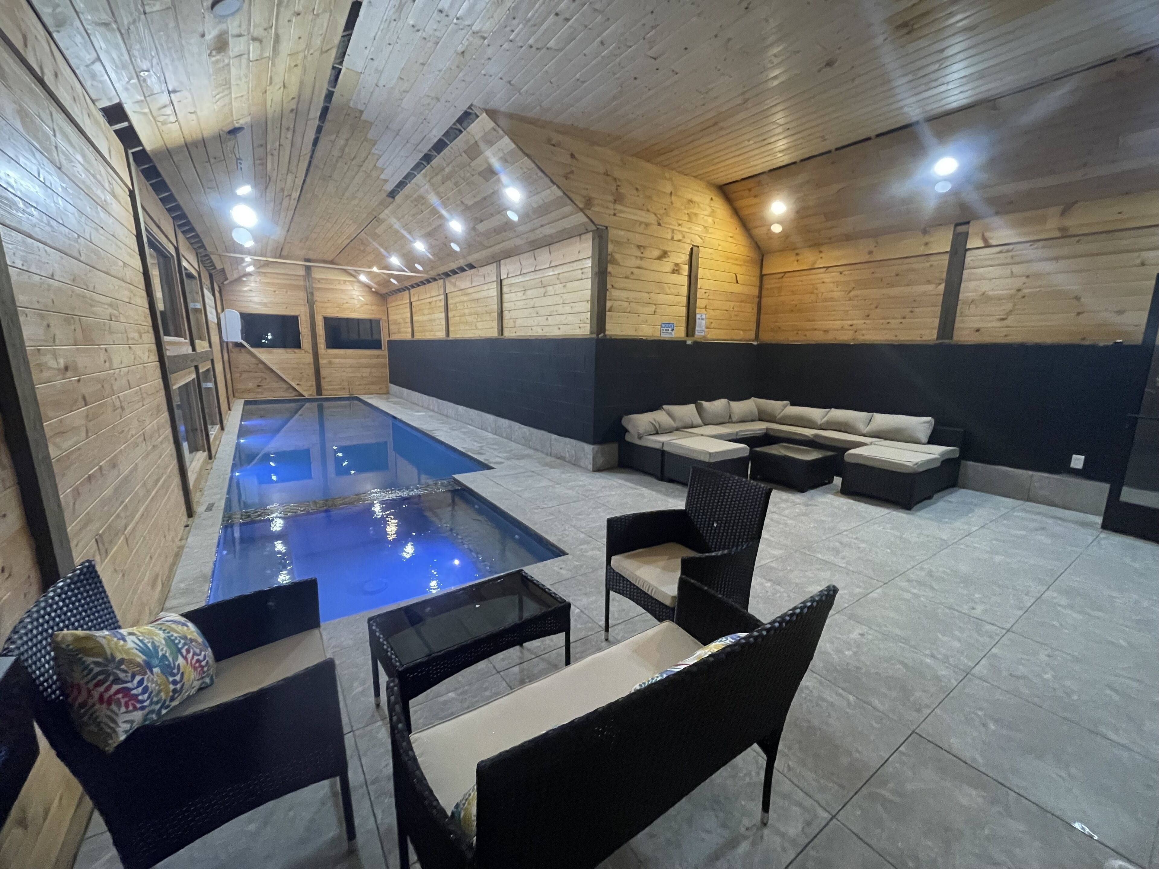 An indoor pool area with a glass floor, a sectional sofa, and black wicker chairs.
