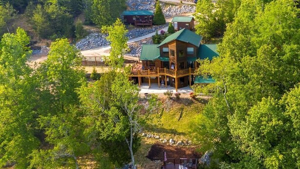 Una cabaña con terraza con vista a un lago, rodeada de un bosque denso.
