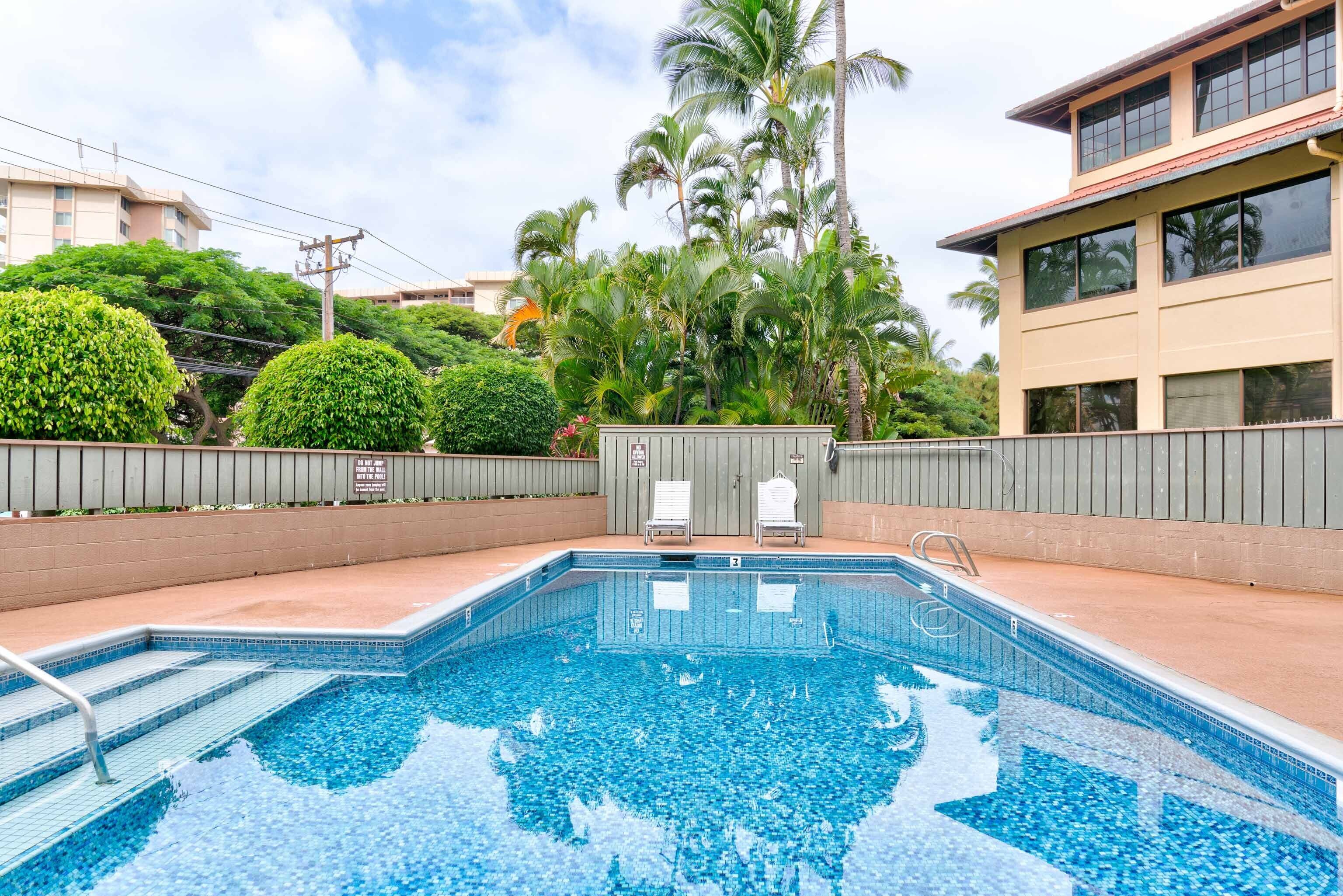 A swimming pool with steps leading into it, surrounded by greenery and a building with large windows.