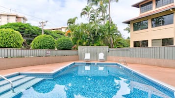 A swimming pool with steps leading into it, surrounded by greenery and a building with large windows.