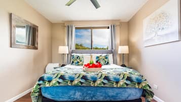 Ein Schlafzimmer mit einem großen Bett, einem Deckenventilator, einem Fenster mit Vorhängen, einem Nachttisch und einem an der Wand befestigten Spiegel.