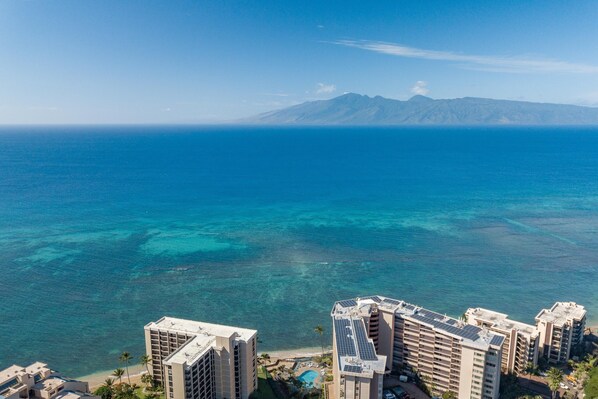 A high-rise hotel with multiple floors, a pool, and a view of the ocean and mountains in the background.