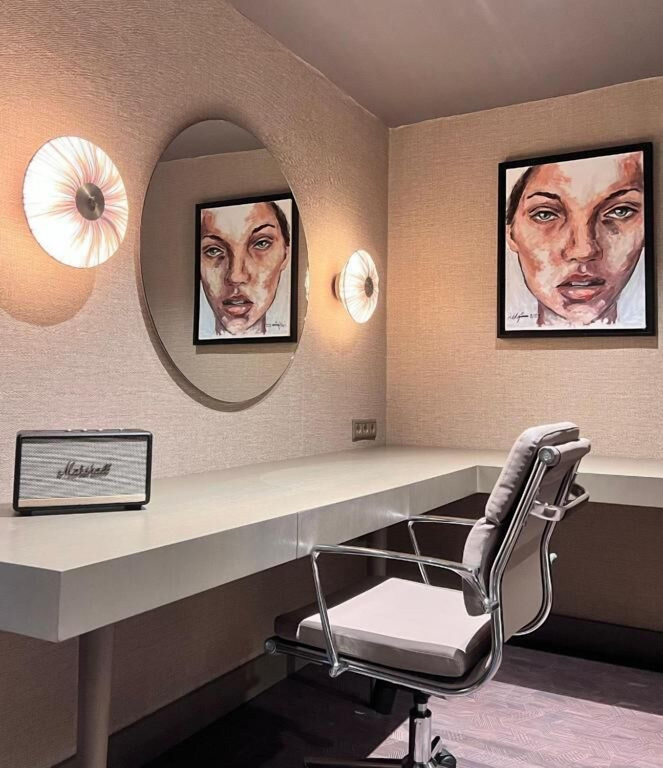 A modern office space with a curved desk, a high chair, and two framed artworks on the wall.
