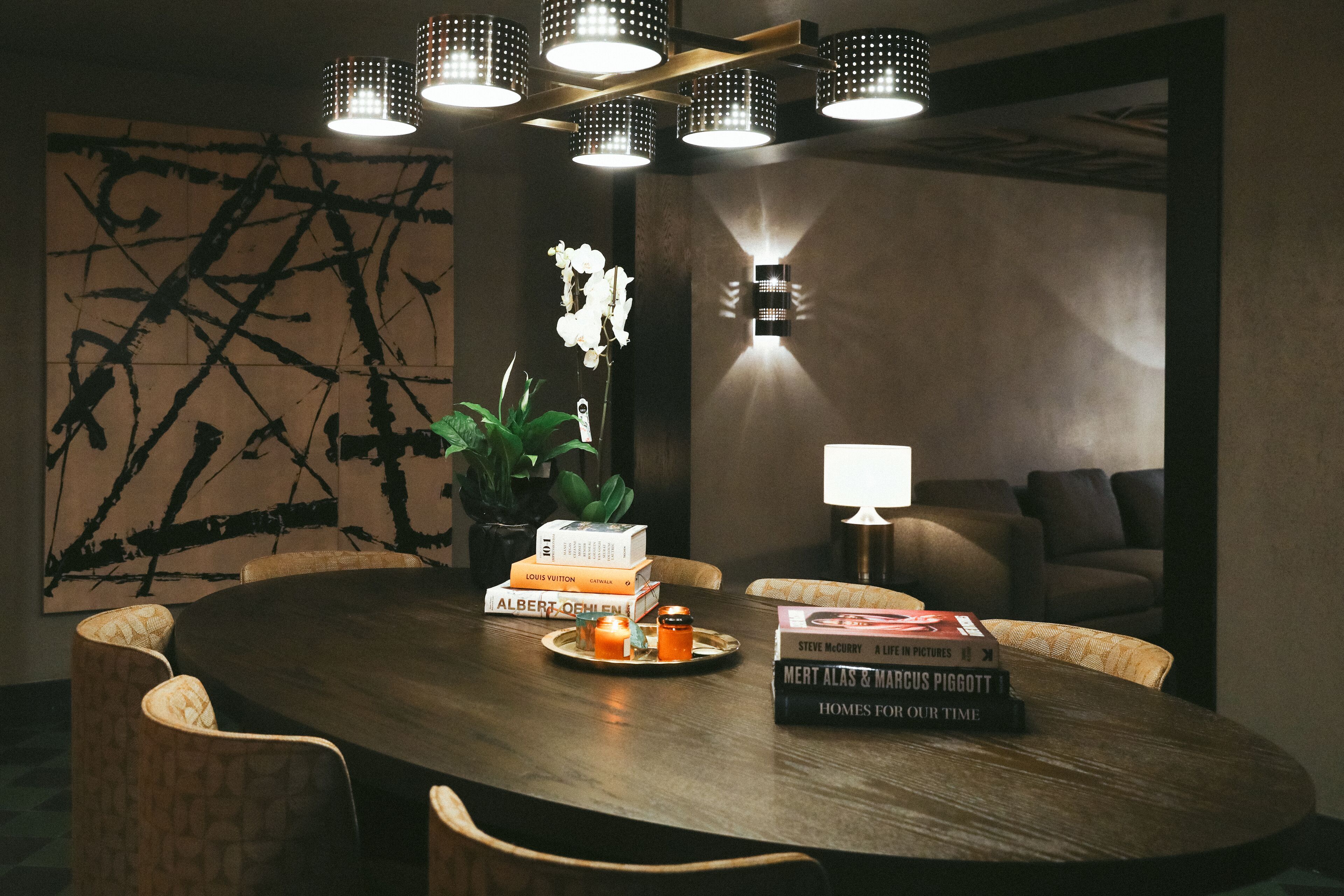 A modern dining area with a round table, books, candles, and a potted plant.