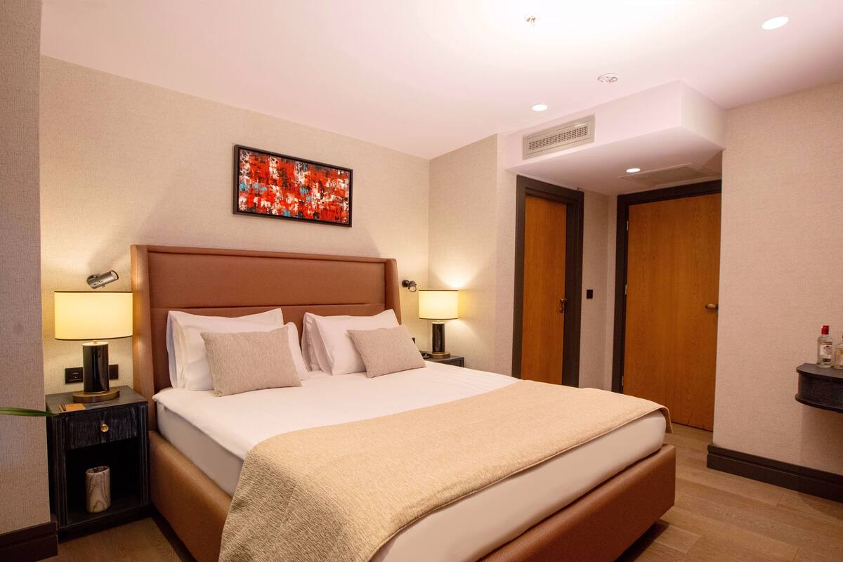 A hotel room with a large bed, two bedside tables with lamps, a wall-mounted artwork, and a door.