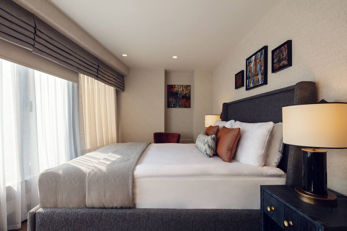 A hotel room with a large bed, a bedside table with a lamp, a chair, and artwork on the wall.
