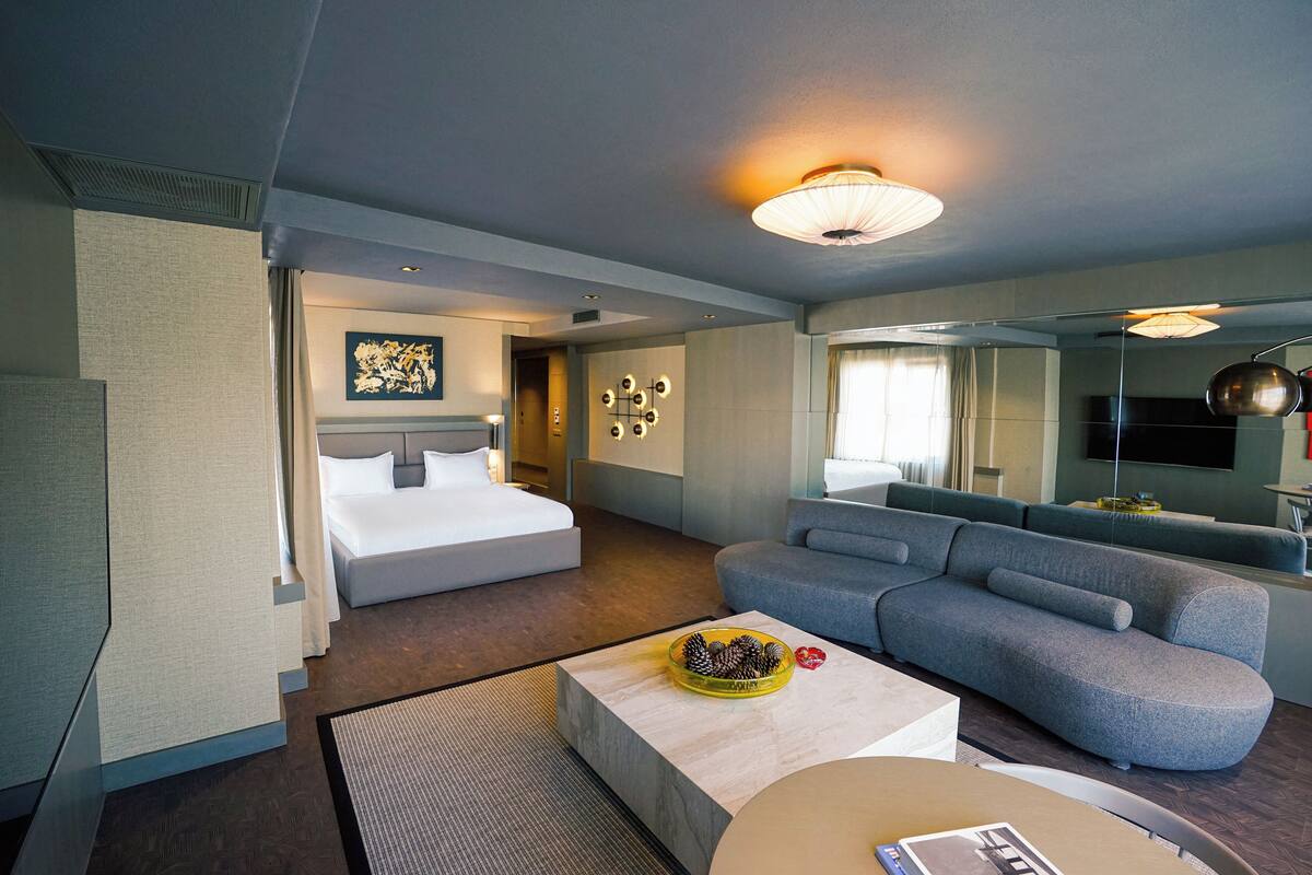 A modern hotel room with a bed, sofa, and a coffee table.