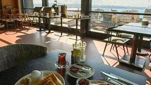 A dining area with a table set for a meal, large windows with a city view, and a cozy seating arrangement. - Root Karaköy Bosphorus Hotel & Spa (Istanbul)