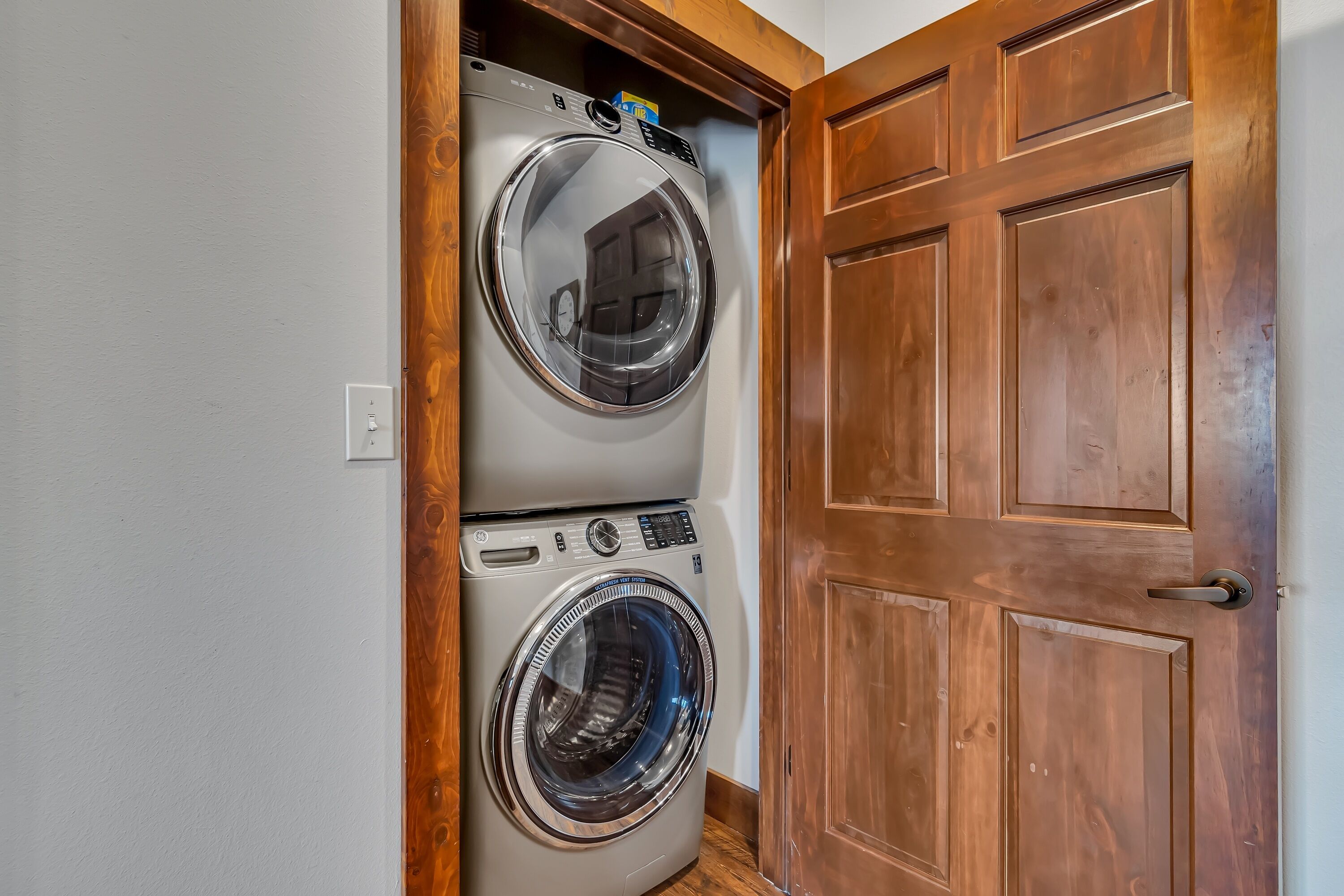 A laundry room with two stacked front-loading washing machines and a wooden door.