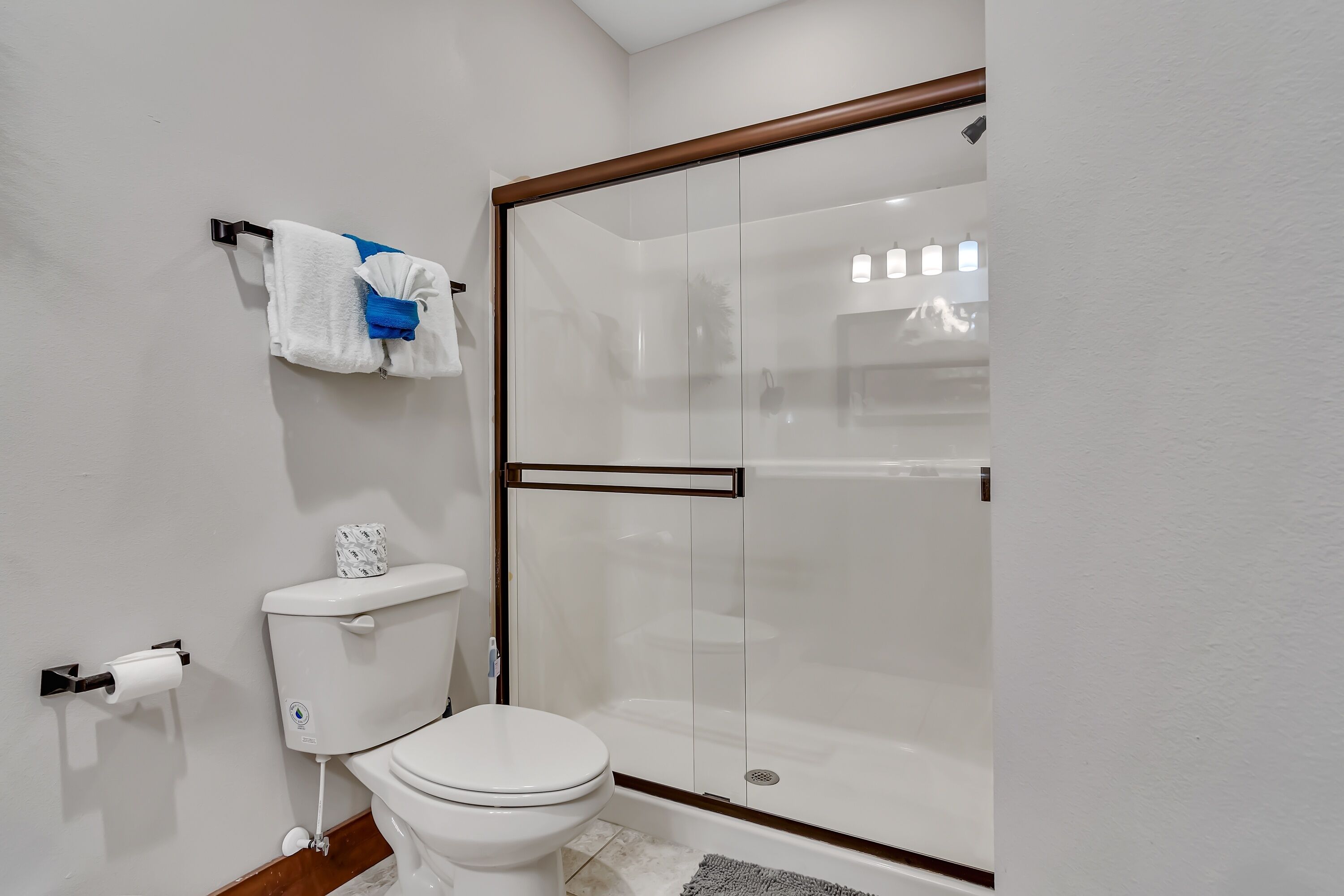 A modern bathroom with a toilet, a glass-enclosed shower, and a towel rack with a blue towel.