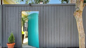Une clôture en bois grise avec une porte de couleur turquoise, un pot de fleurs et le numéro « 222 » sur le côté gauche.
