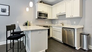 Une cuisine moderne avec des meubles blancs, un îlot central, des appareils en acier inoxydable et des luminaires suspendus.