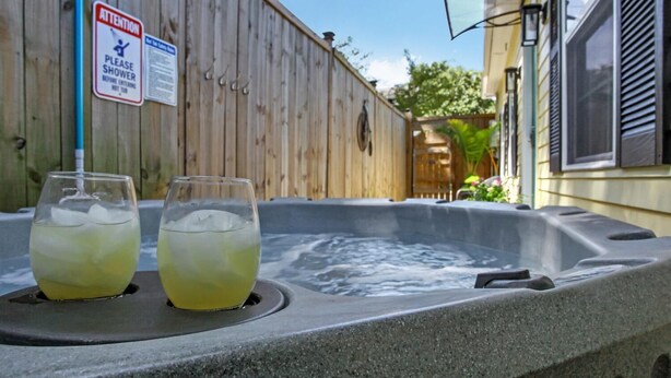 Un bain à remous avec deux verres d’une boisson jaune, une clôture en bois et un panneau indiquant qu’il faut prendre une douche avant d’y entrer.