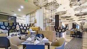 A modern restaurant with high ceilings, hanging light fixtures, and a central seating area with tables set for dining. - Hotel Royal Beach 5 Premium - Central Sea View G6 (Sunny Beach)
