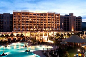 A hotel with a large pool area, multiple balconies, and a well-lit facade.