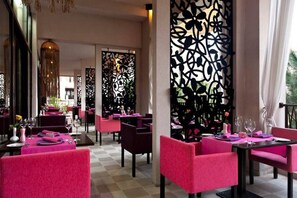 A restaurant with pink chairs and tables, decorative black panels, and a checkered floor.