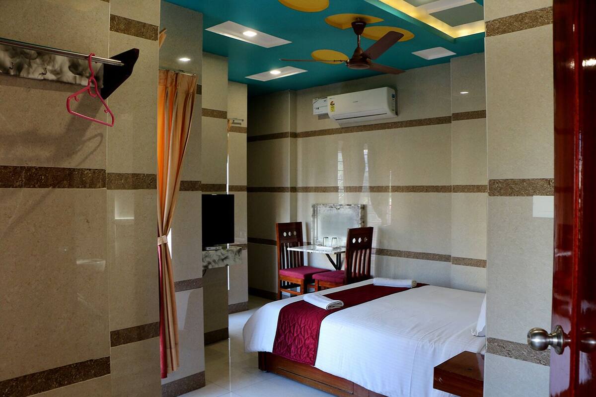 A hotel room with a bed, a desk, a chair, a television, and an air conditioning unit.