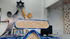 A hotel reception area with a modern design, featuring a star-shaped ceiling light, a reception desk with a unique geometric pattern, and a ceiling fan. - Hotel Blue Stone (Puducherry)