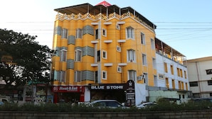 A multi-story hotel with a yellow facade, balconies, and a sign for 'Hotel Blue Stone' indicating it has rooms, banquet hall, and a restaurant. - Hotel Blue Stone (Puducherry)
