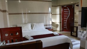 A hotel room with a large bed, a wooden headboard, a red throw blanket, and a wooden nightstand. - Hotel Blue Stone (Puducherry)