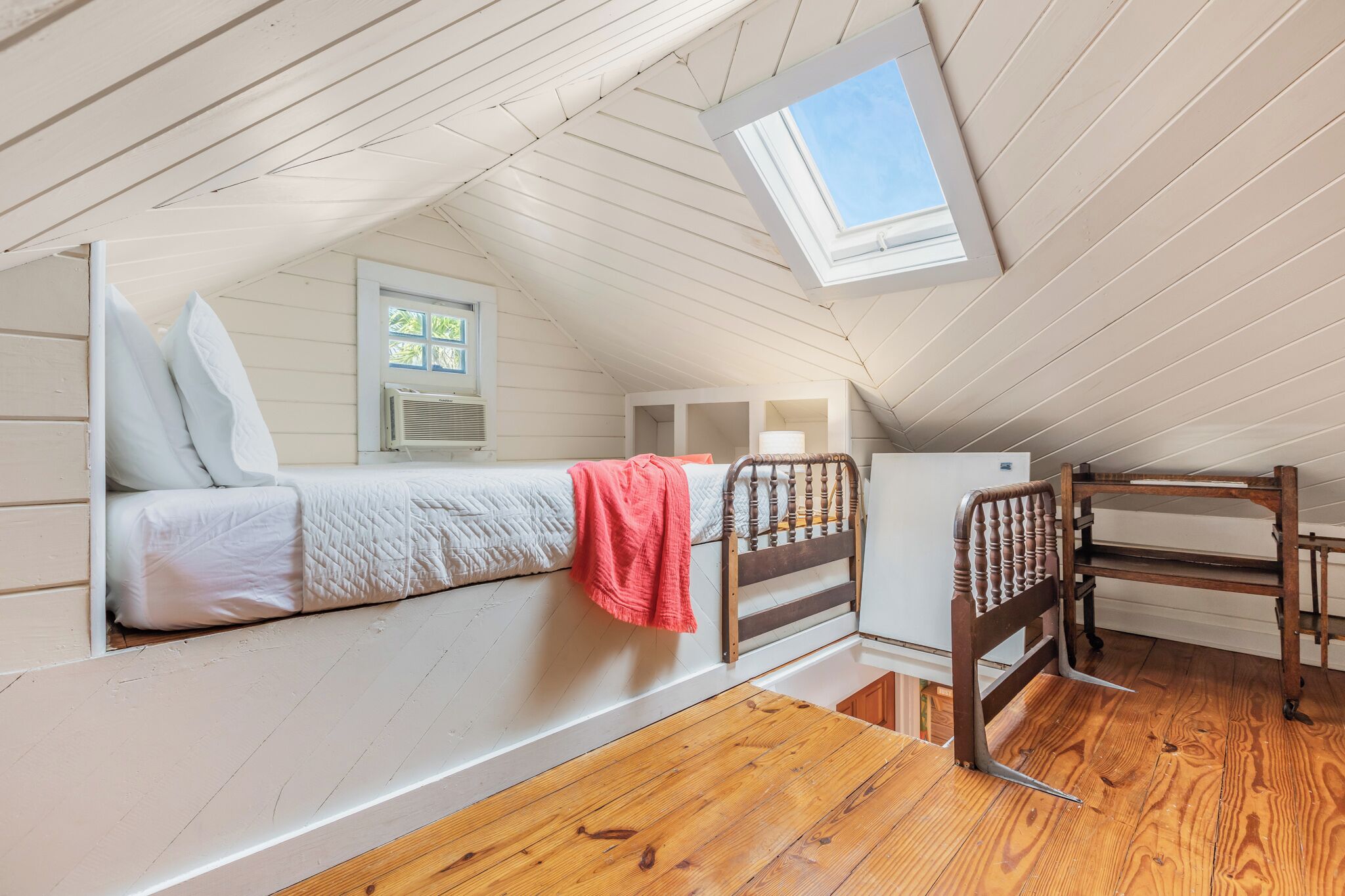 A dormitory-style room with a bunk bed, a desk, a chair, and a skylight.
