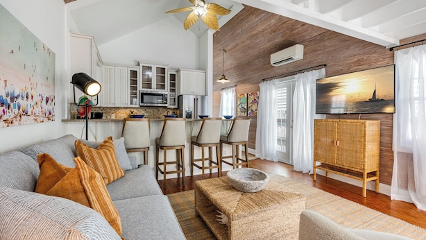 Un salon moderne avec un canapé, des fauteuils et une table basse. Il y a également un coin cuisine équipé de placards et d’appareils électroménagers, ainsi qu’un balcon avec vue sur la mer.