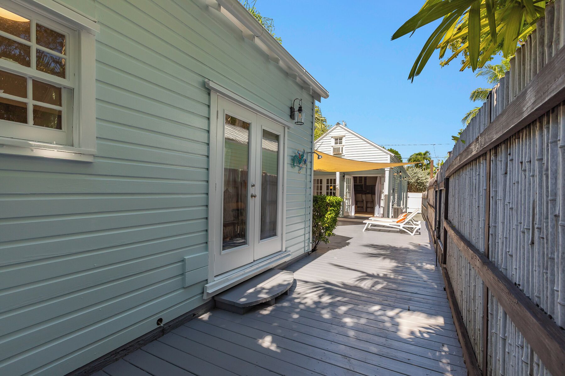 A narrow wooden deck with a covered patio area, a small outdoor seating area, and a wooden fence.