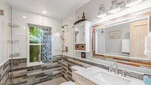 Une salle de bain moderne avec une douche à l’italienne en verre, un grand miroir et un lavabo blanc doté d’un plan de toilette en marbre.