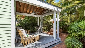 Une terrasse extérieure couverte, aménagée avec des meubles en osier et dotée d’un barbecue.