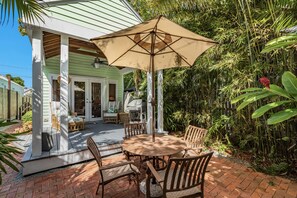Une terrasse avec une table ronde et des chaises, un grand parasol et un espace barbecue.