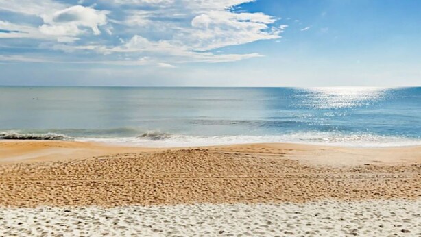 Une plage avec un large rivage sablonneux et une mer calme.