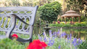 Un parc avec un banc, un kiosque et un étang orné de fleurs.
