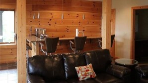 Una habitación acogedora con un sofá de cuero negro, paredes de madera, un comedor con sillas y una pequeña mesa redonda.