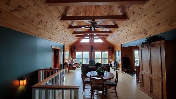 Una habitación amplia con techo de madera, un comedor con mesa y sillas redondas, y vistas al exterior a través de grandes ventanales.