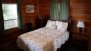 Un dormitorio de cabaña de madera con cama, mesita de noche, lámpara y ventana con cortinas.