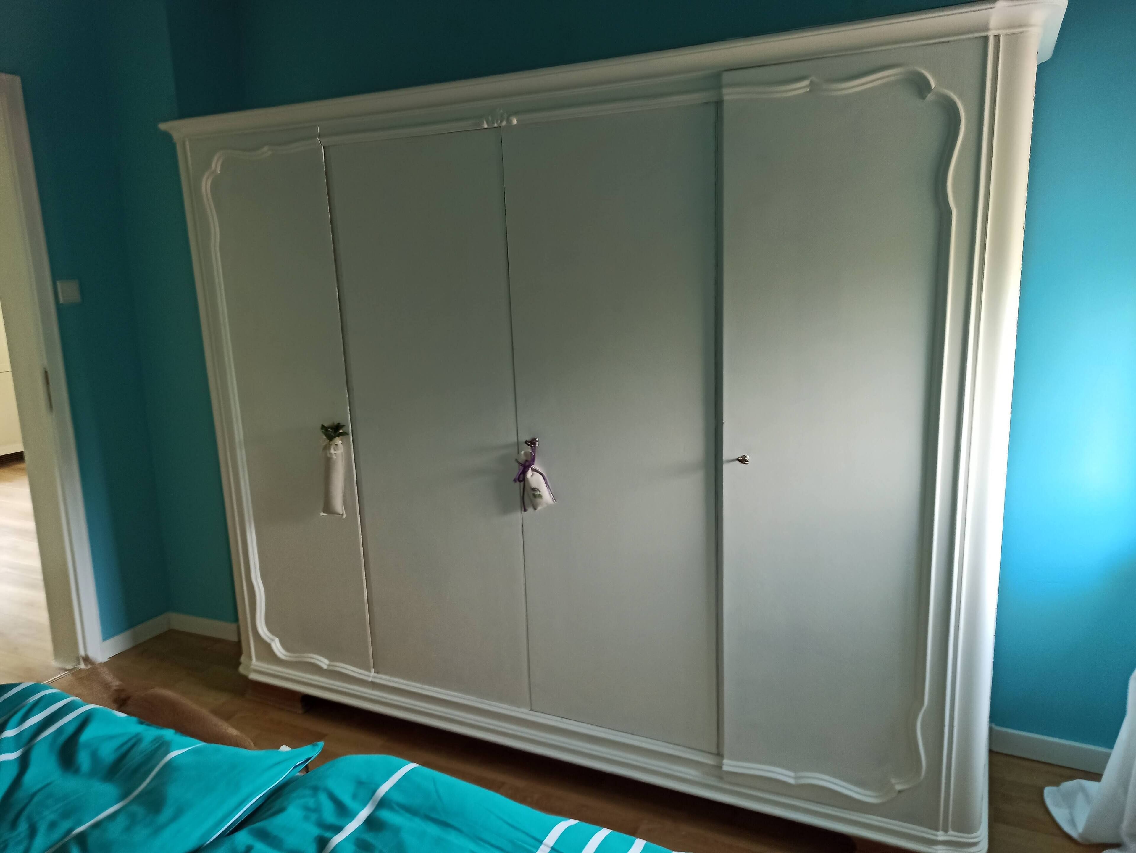 A large wardrobe with two doors and a handle, a bed with a teal bedspread, and a wooden floor.