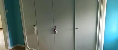 A large wardrobe with two doors and a handle, a bed with a teal bedspread, and a wooden floor.