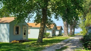 A row of small, light blue cabins with a gravel path leading to them, surrounded by lush greenery and trees.