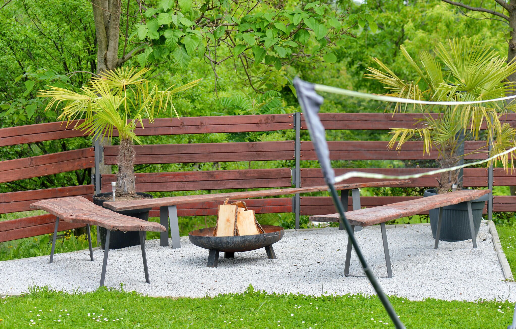 Un banc en bois avec un foyer au centre, entouré de gravier et de verdure.