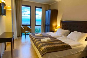 Une chambre d’hôtel avec un grand lit, une chaise, un bureau et une vue sur la mer par les fenêtres.