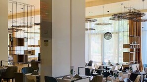A modern restaurant interior with high ceilings, pendant lighting, and a mix of seating arrangements.