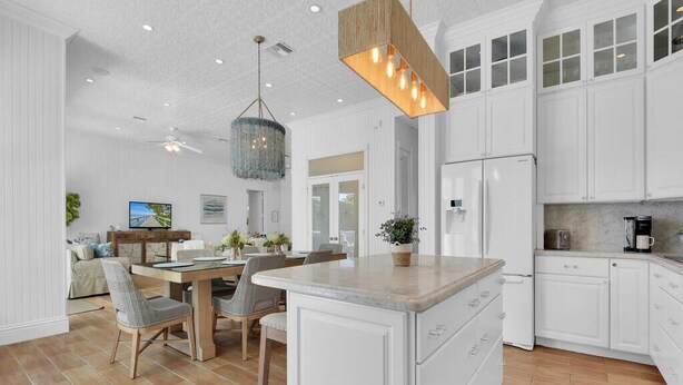 A spacious kitchen with white cabinetry, a central island, and a dining area with a wooden table and chairs. - NEAPOLITAN SKY - Key West Style Home in Olde Naples (Naples)