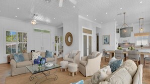 A spacious living room with a large sofa, a coffee table, and a dining area with chairs and a table. - NEAPOLITAN SKY - Key West Style Home in Olde Naples (Naples)