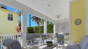 A covered outdoor seating area with white furniture and a yellow wall. - NEAPOLITAN SKY - Key West Style Home in Olde Naples (Naples)