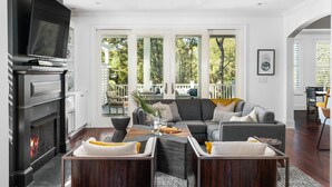 A modern living room with a fireplace, a large flat-screen TV, and a comfortable seating area with a sofa and chairs. - Modern coastal retreat steps from Center Street and the beach (Folly Beach)