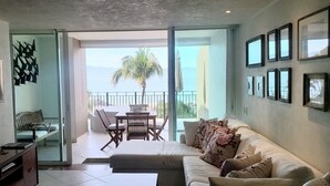 A modern living room with a sofa, a TV, and a dining area with a table and chairs. - Beachfront 1 br. condo with private hot tub at Gran Venetian Puerto Vallarta (Puerto Vallarta)