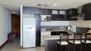 A modern kitchen with dark cabinets, a white refrigerator, a microwave, a stove, and a bar area with two chairs. - Beachfront 1 br. condo with private hot tub at Gran Venetian Puerto Vallarta (Puerto Vallarta)
