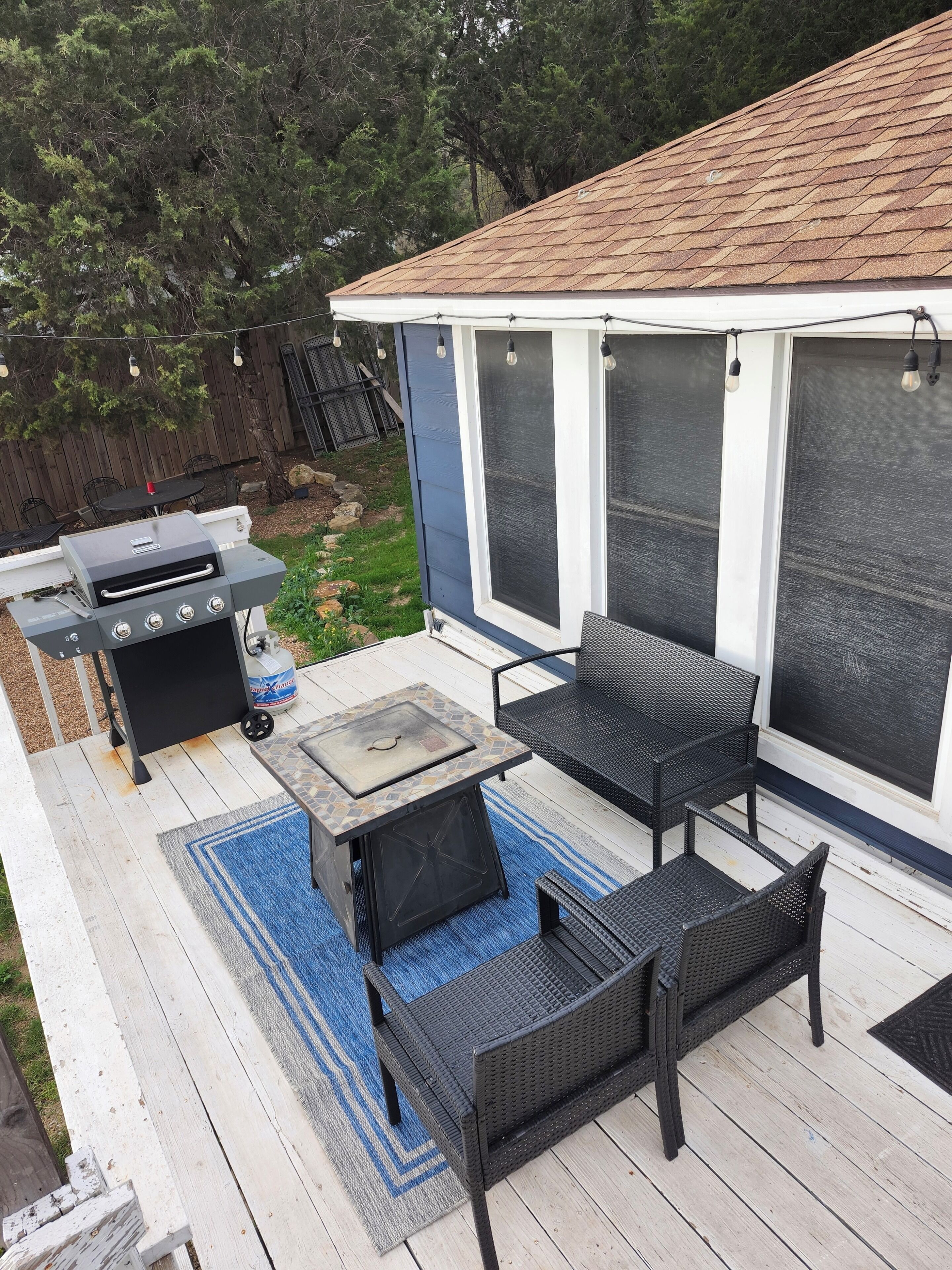 A covered outdoor patio with a grill, seating, and a view of the backyard.